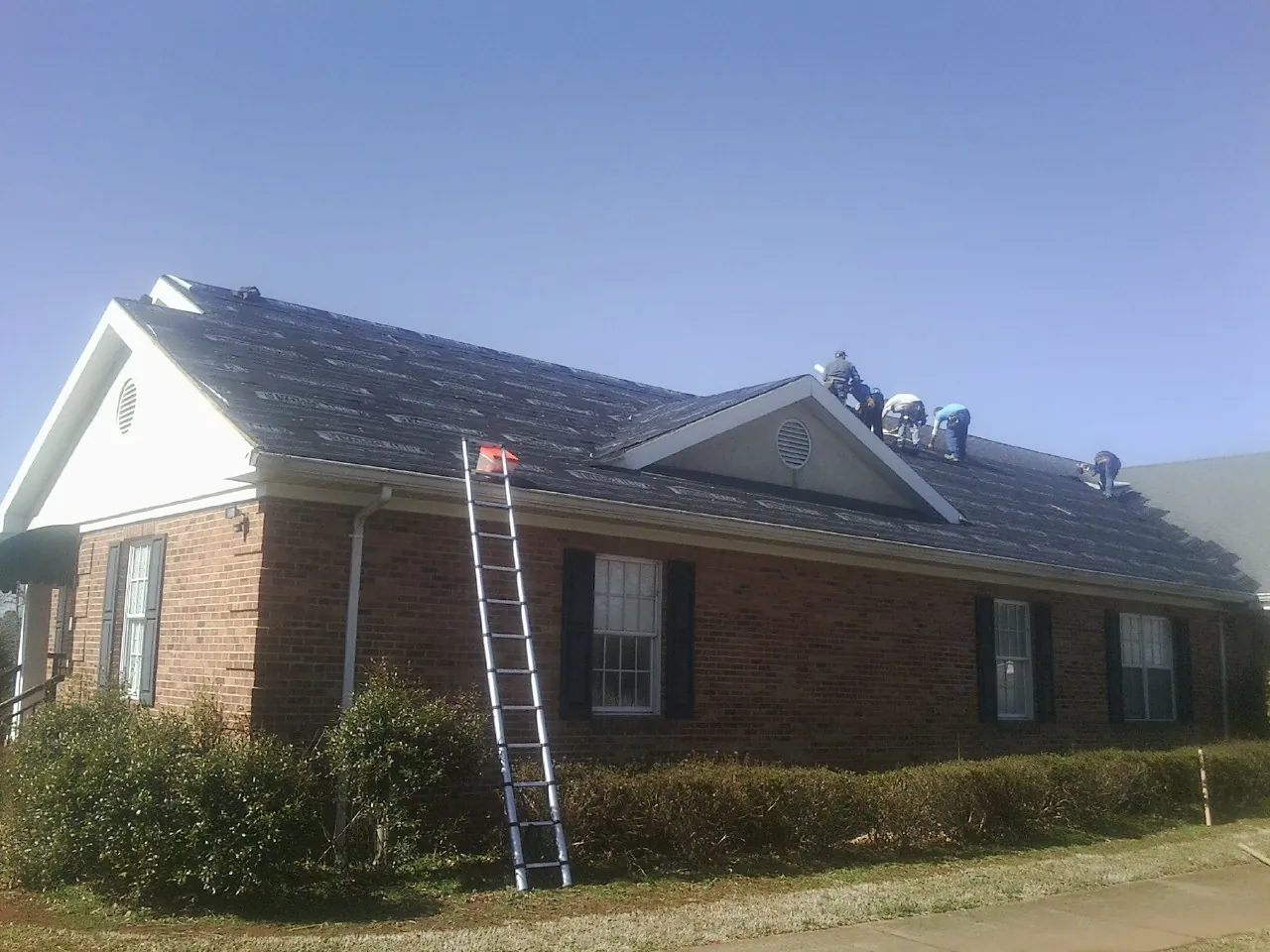 Crew tearing shingles off a brick ranch roof with a ladder set — Emergency Roof Repair work by our crew in Villa Park
