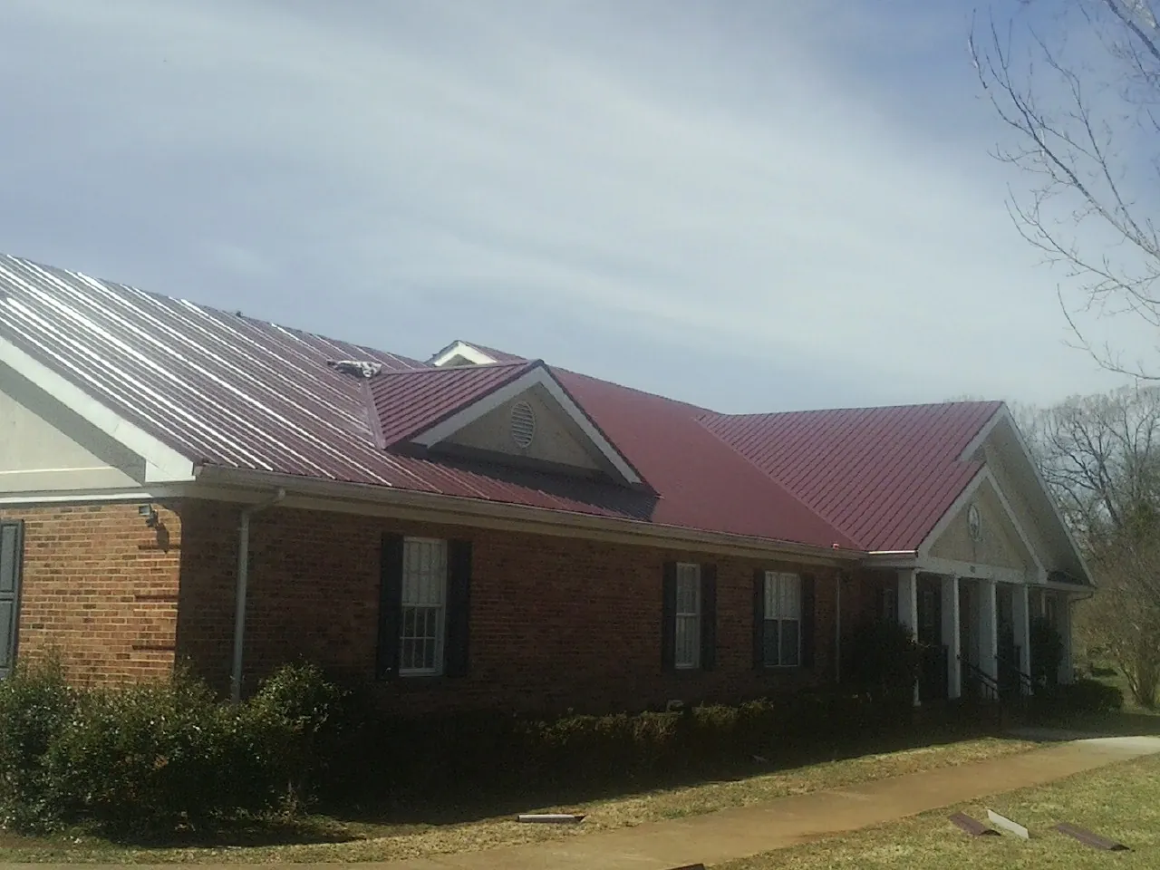 Red metal roof with gabled entries on a long brick building, from a Hail Damage Roof Repair job in Villa Park